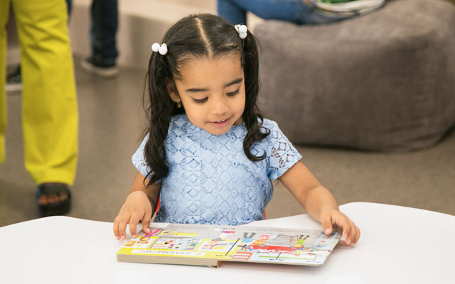 Niña sonríe mientras observa un libro en el Centro Cultural de Buenaventura