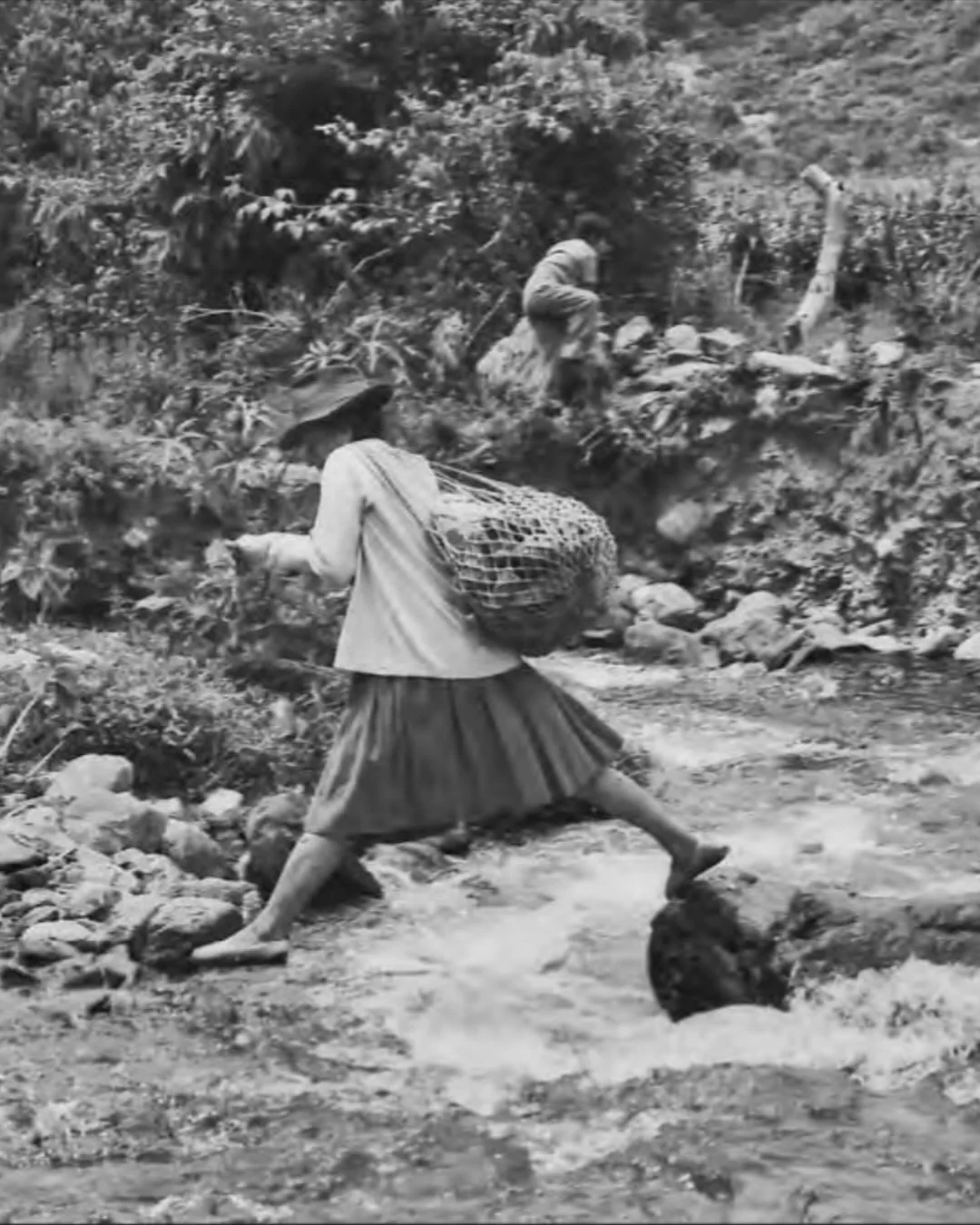 Foto a blanco y negro, de una campesina, pasando un río 