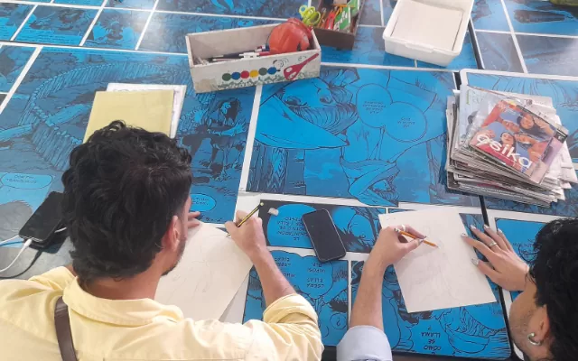 2 personas dibujando fanzines sobre un fondo azul 