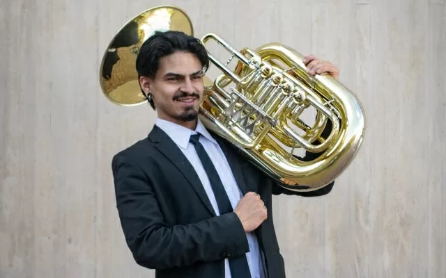 Músico en plano medio, sonriendo y sosteniendo una tuba 