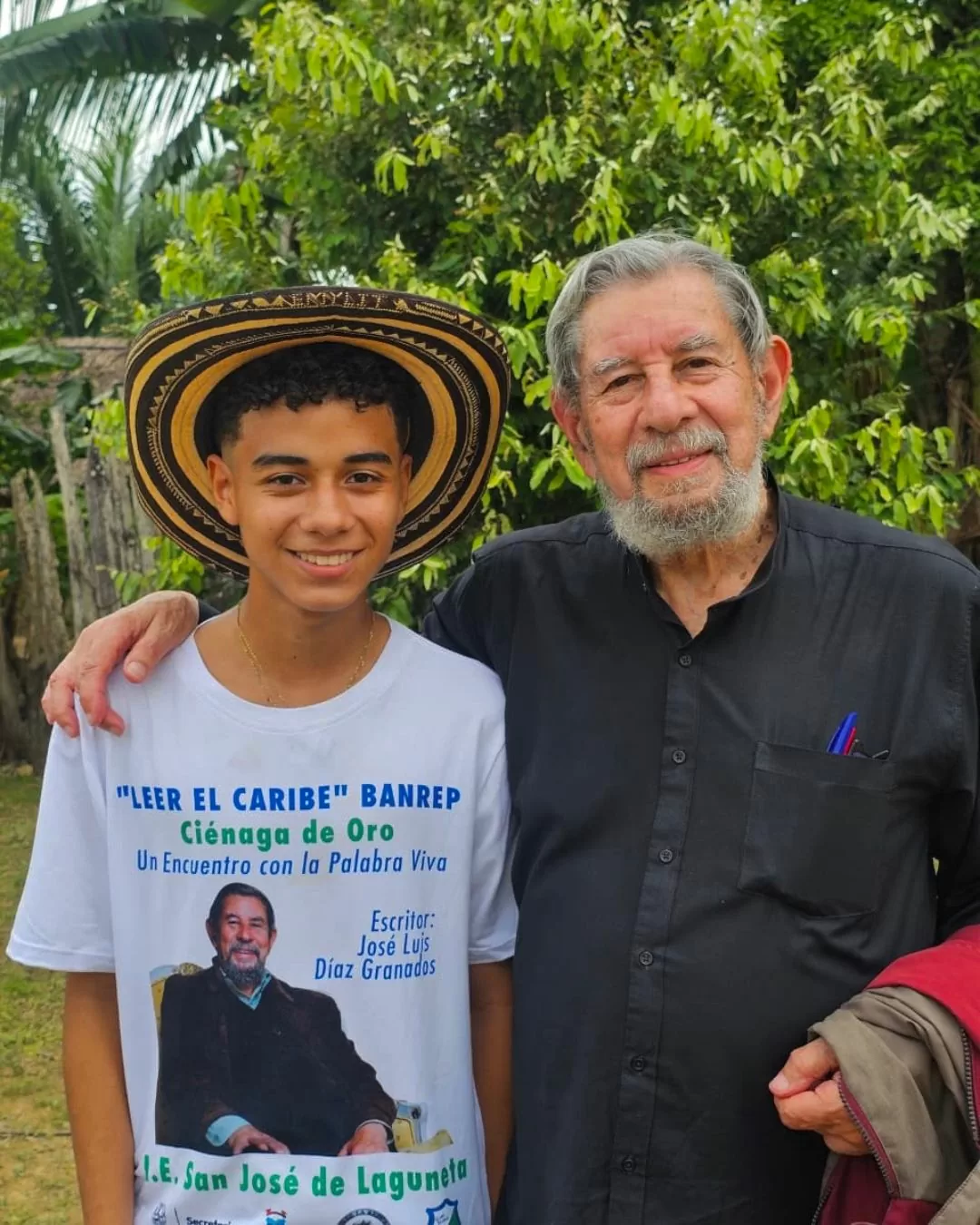 Foto a color de Jose Luis Diazgranados junto a un joven, utilizando un sombrero y una camiseta con el rostro del escritor 