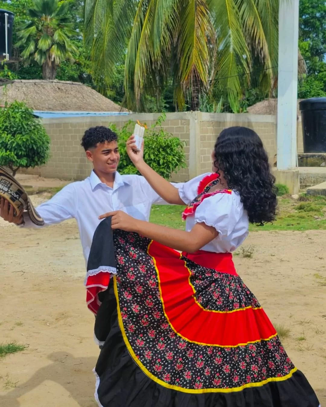 Un joven vestido de blanco, y una joven utilizando falta negra con toques rojos, bailando como parte de las actividades de Leer el Caribe 