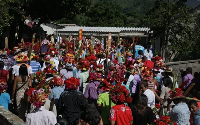 Grupo de personas caminando de espaldas ataviados con sombreros de flores 