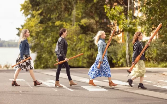 Cuatro mujeres sosteniendo sus flautas dulces mientras cruzan la cebra de una calle 