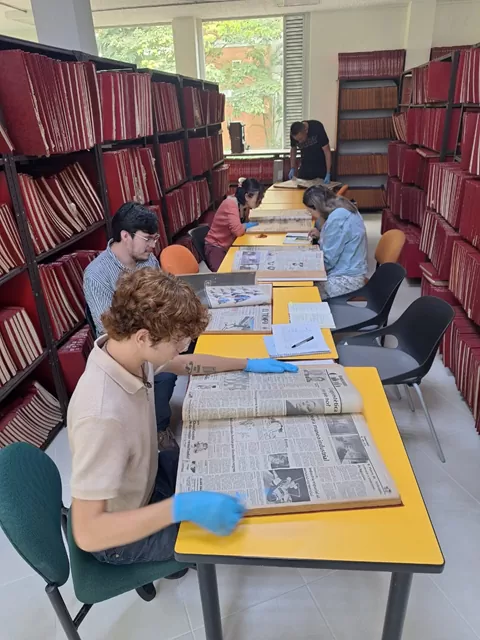 Fotografía de un grupo de personas pertenecientes a la comunidad de aprendizaje en torno a la colección fotográfica Carlos Eslava Flórez consultando prensa en la biblioteca