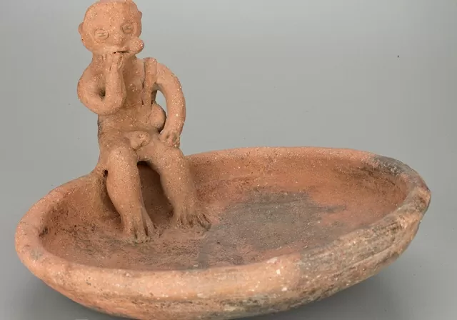 Una plato hecho en cerámica con un personajes sentado en el borde