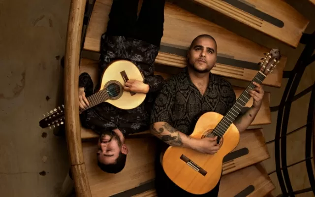 Dos músicos recostados sobre unas escaleras cafés tocando la bandola y la guitarra 