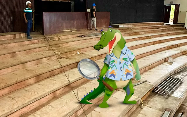 Emiro, el caimán ilustrado, con una lupa en la obra del teatro Amira de la Rosa