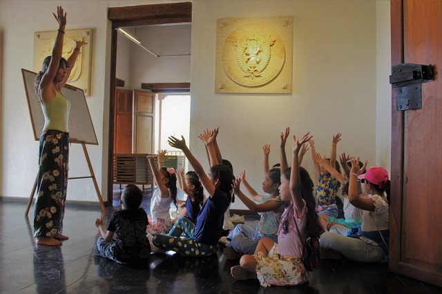 Grupo de niños y niñas sentados con los brazos levantados 