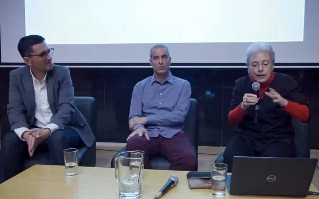 Nicolas Gómez, Juan Fernando Herrán y María Margarita Malagón, sentados uno junto al otro, con una pantalla detrás, hablando hacia el publico 