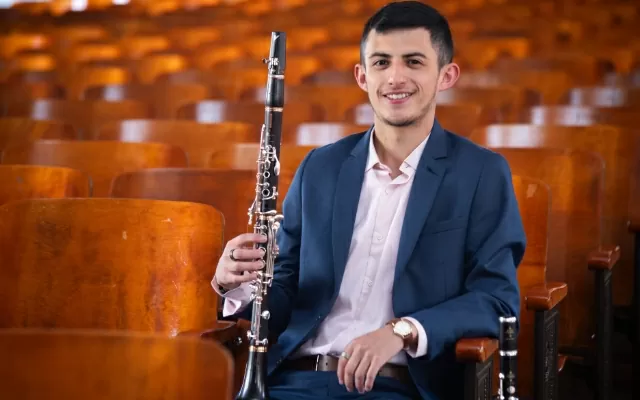 Hombre sentado en un auditorio, mirando fijamente, sonriendo y sosteniendo el clarinete 