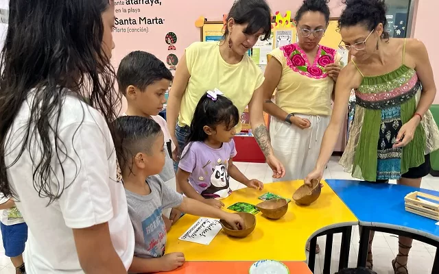 Grupo de niños y de adultos alrededor de una mesa donde hay semillas de cilantro, orégano y arroz 