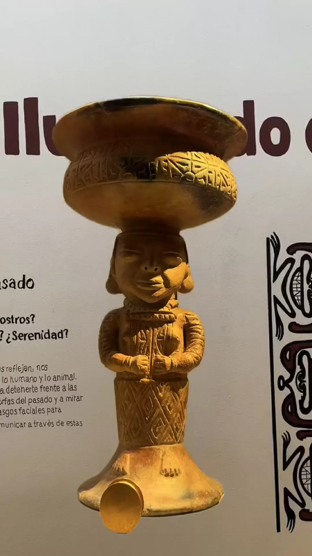 Objeto arqueologico, dorado, sobre un fondo de pared con un impreso, sobre la exposición "Ilustrando el pasado"