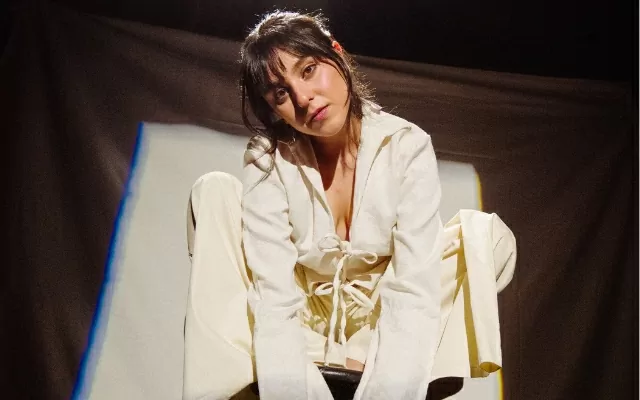 Isabella Ruíz, vestida de blanco, sentada, mirando fijamente 