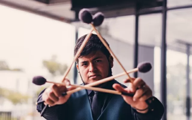 Hombre usando traje negro, sosteniendo un instrumento con sus manos, mientras mira fijamente 