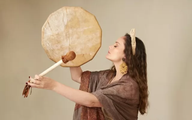 Mujer de perfil, en plano medio, usando un kimono café, tocando un instrumento 