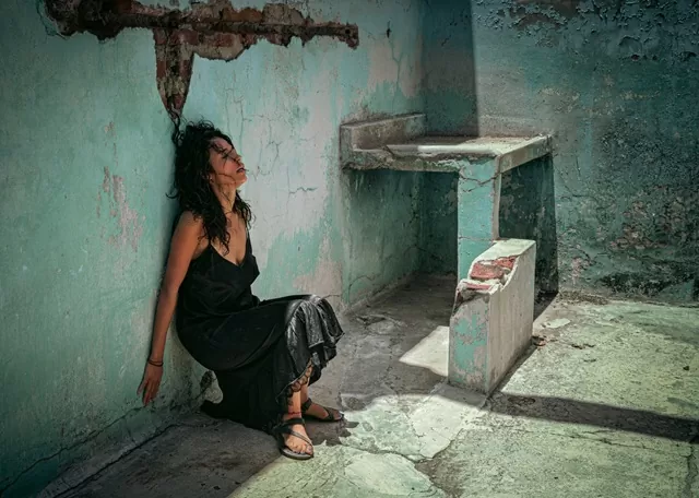 Una mujer vestida de negro recostada sobre una pared en ruinas 