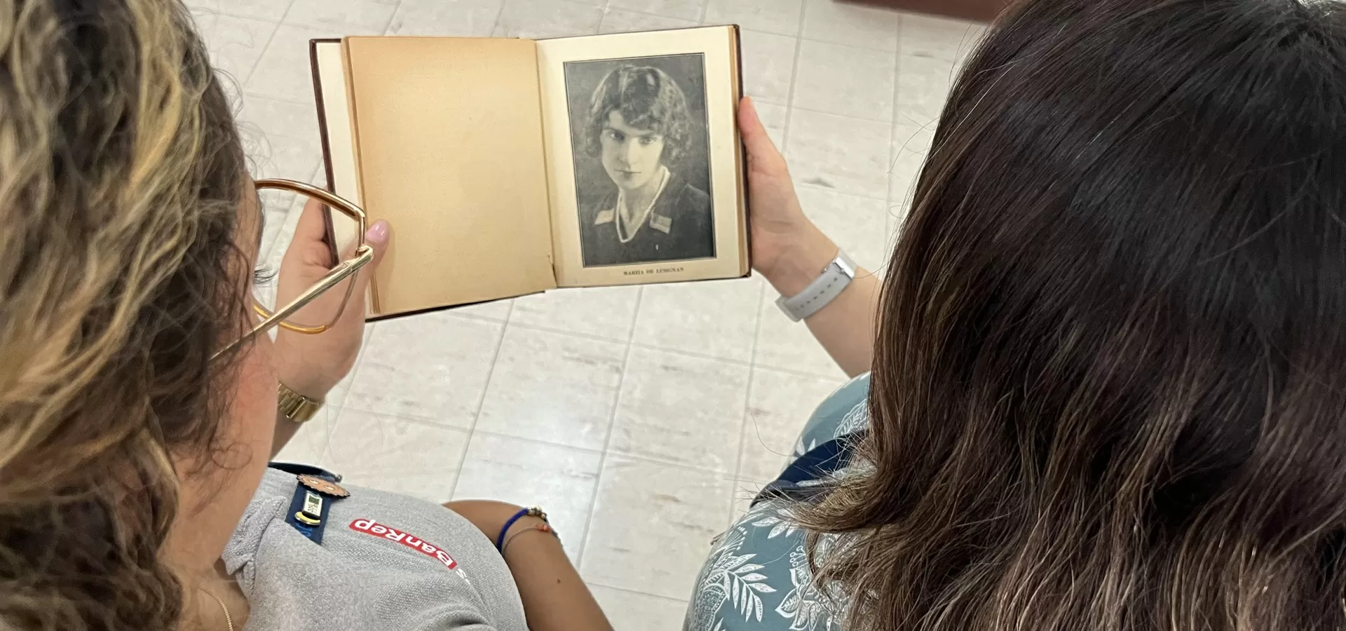 Dos mujeres mirando un libro que contiene una fotografía de una mujer 