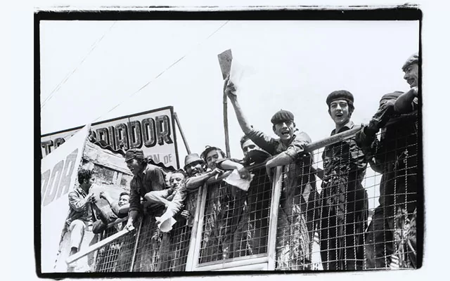 Fotografía en blanco y negro de un grupo de obreros subidos en una reja en actitud de protesta