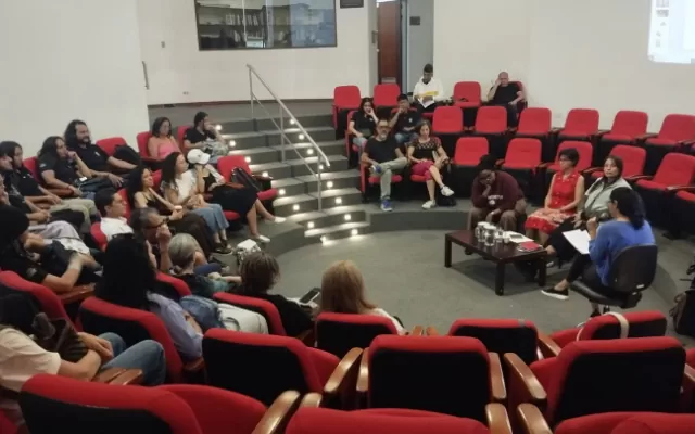 En la foto se aprecia a un grupo de personas que asisten a una conversatorio en la sala de música