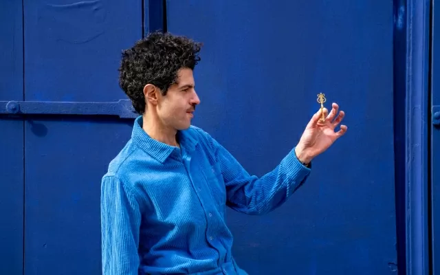 Artista sobre un fondo azul, de perfil, usando una camisa azul, sosteniendo una llave con su mano
