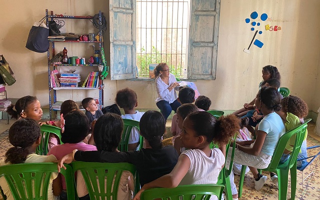 Grupo de niños frente a la tallerista que enseña un libro