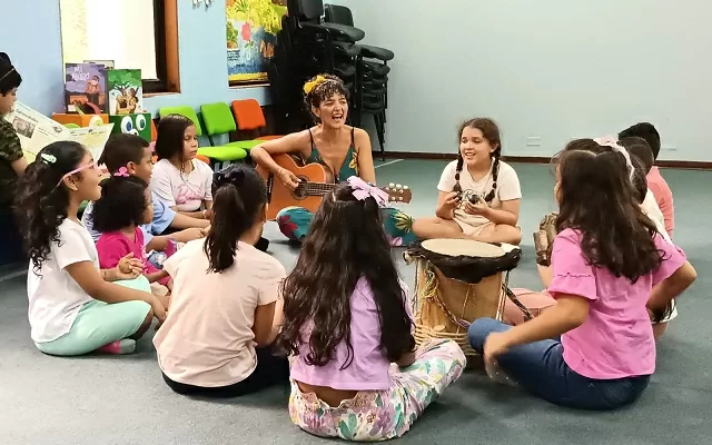 Grupo de niños cantando y una profesora tocando guitarra