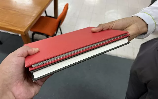 Un libro de pasta roja que pasa de mano en mano 