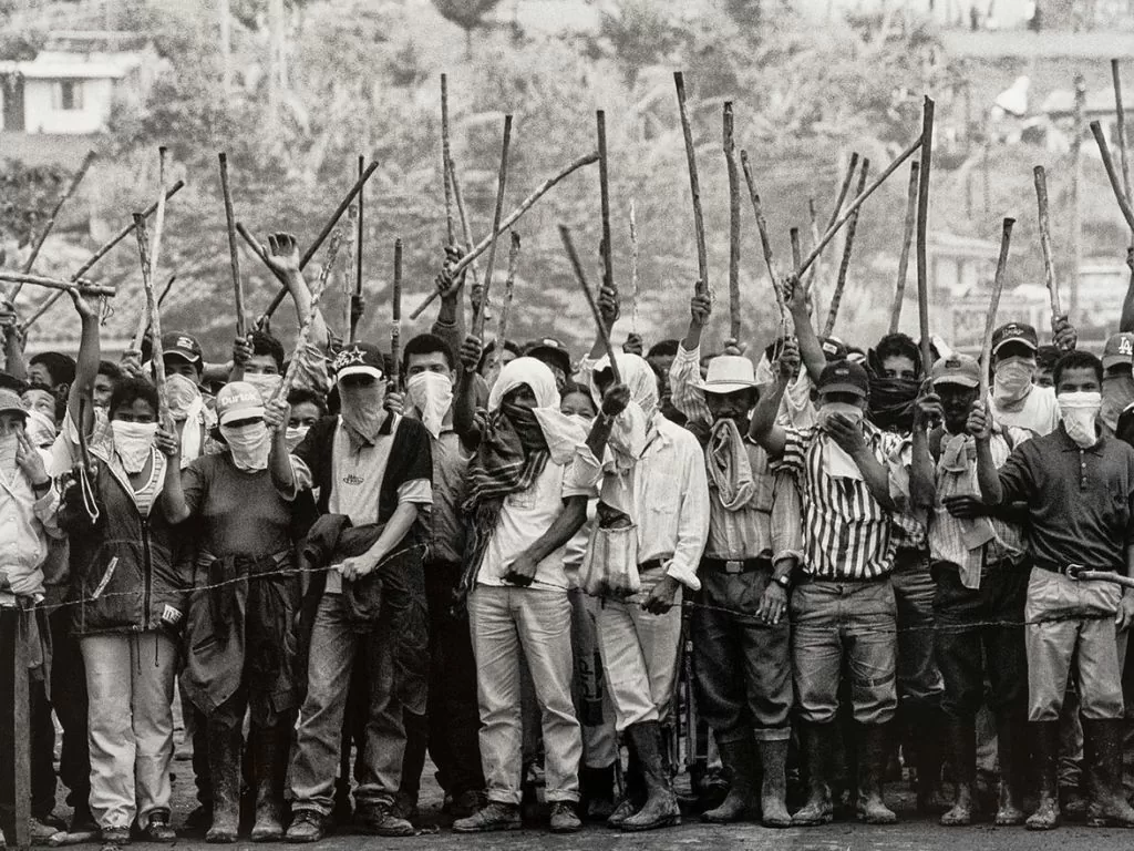 Fotografía en blanco y negro donde se ven varios hombres encapuchados con palos