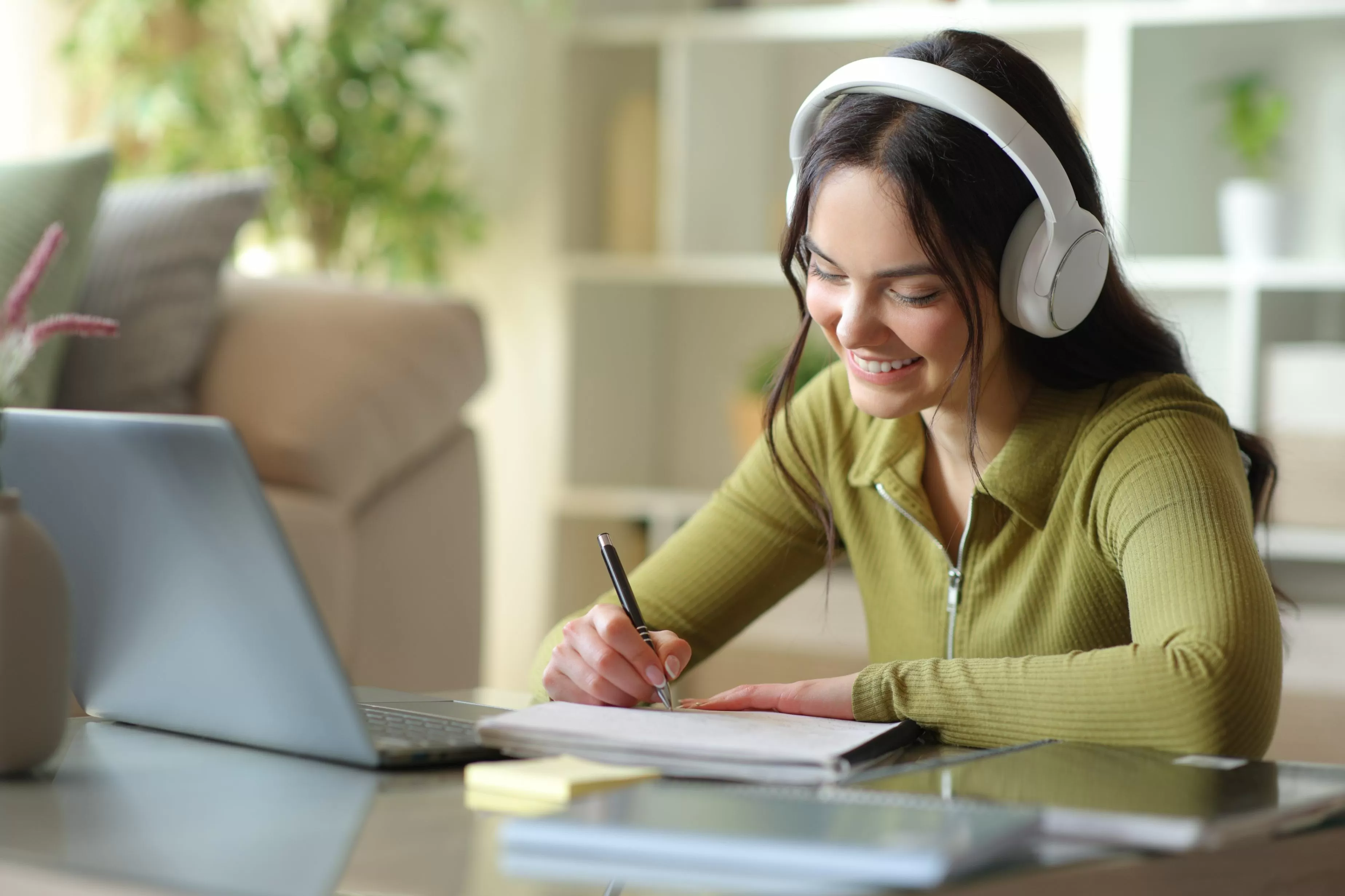 Estudiante feliz que toma las notas que escuchan la lección audio de los auriculares en casa