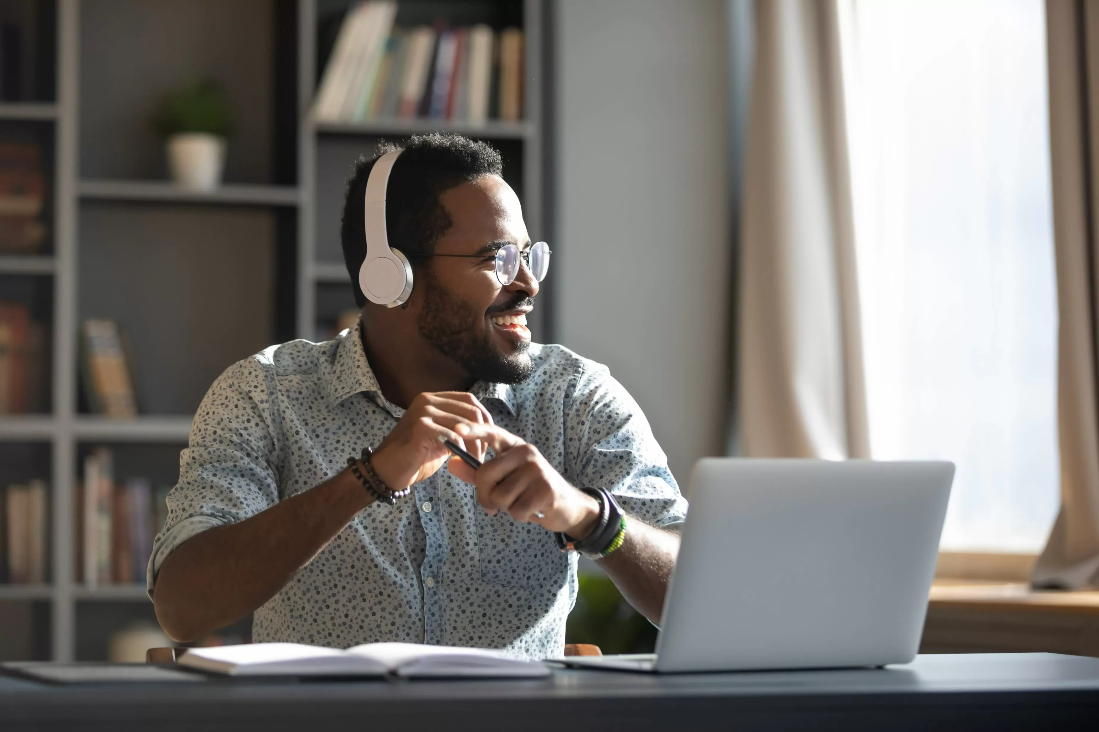 hombre afro sonriente con audífonos, sentado en un escritorio frente a un computador