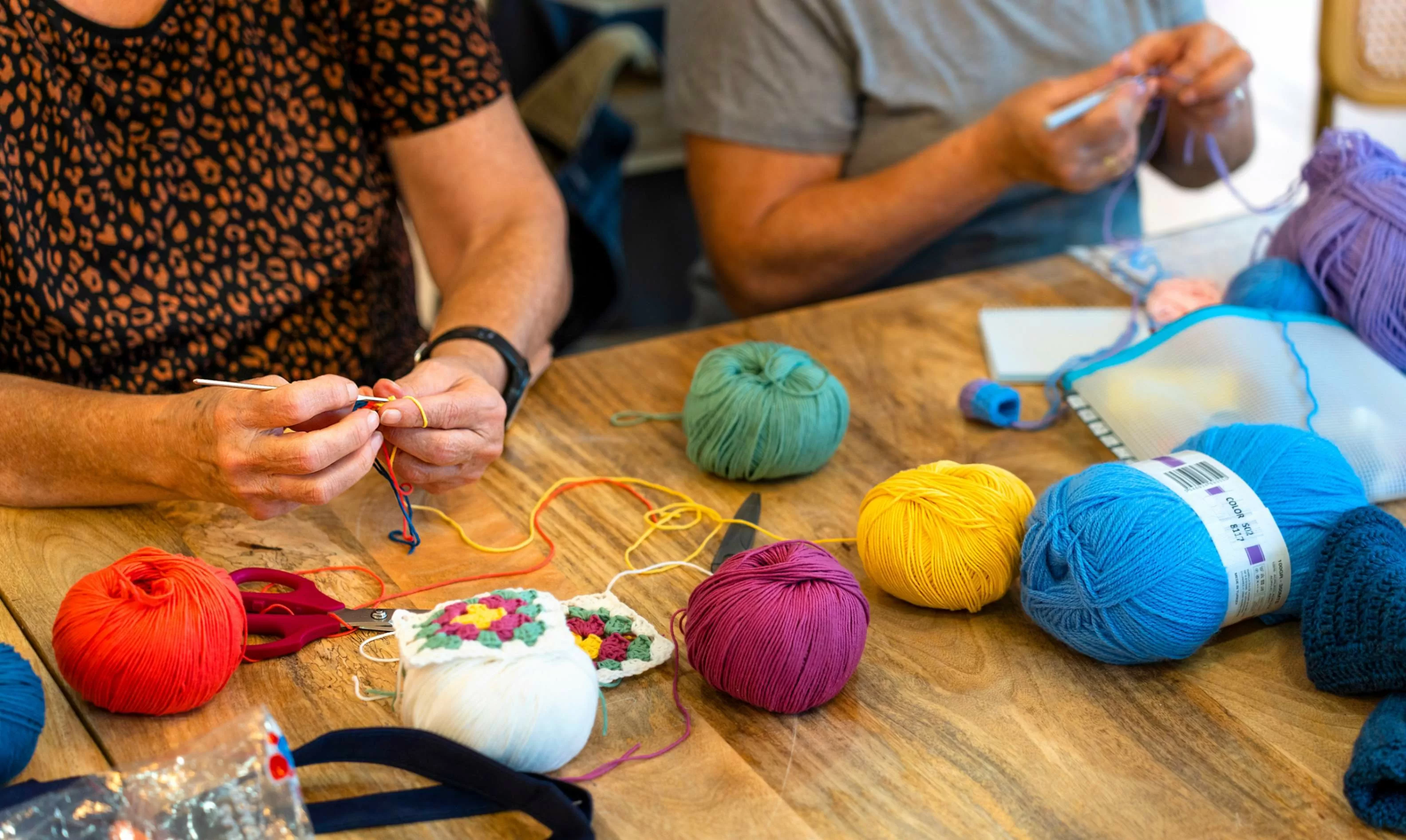 manos de mujeres tejedoras y lanas de varios colores sobre una mesa de madera