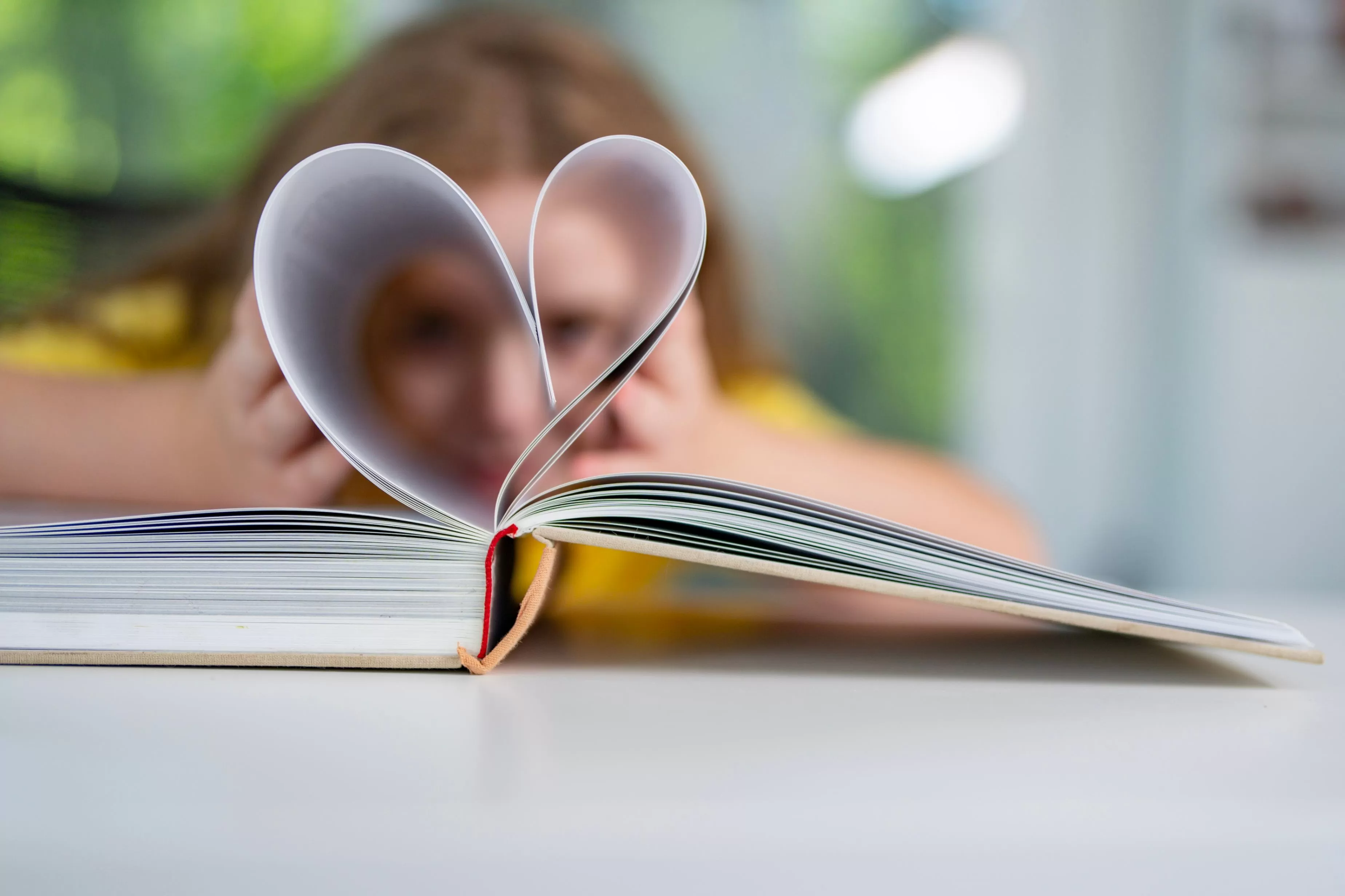 corazón hecho con hojas de un libro, al fondo se ve una niña sonriente