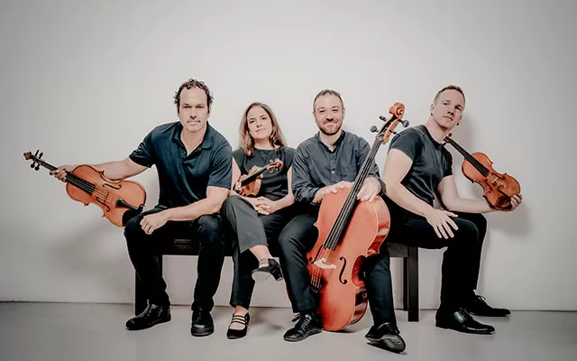 Integrantes del Cuarteto Mivos sentados en una banca con sus instrumentos en las manos