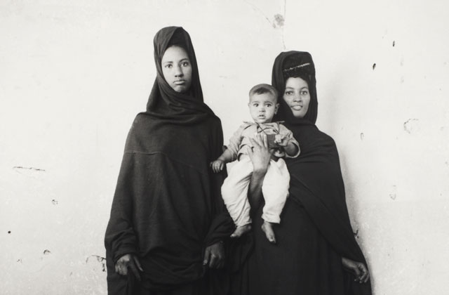 Dos mujeres vestidas de negro sostienen a un niño de blanco