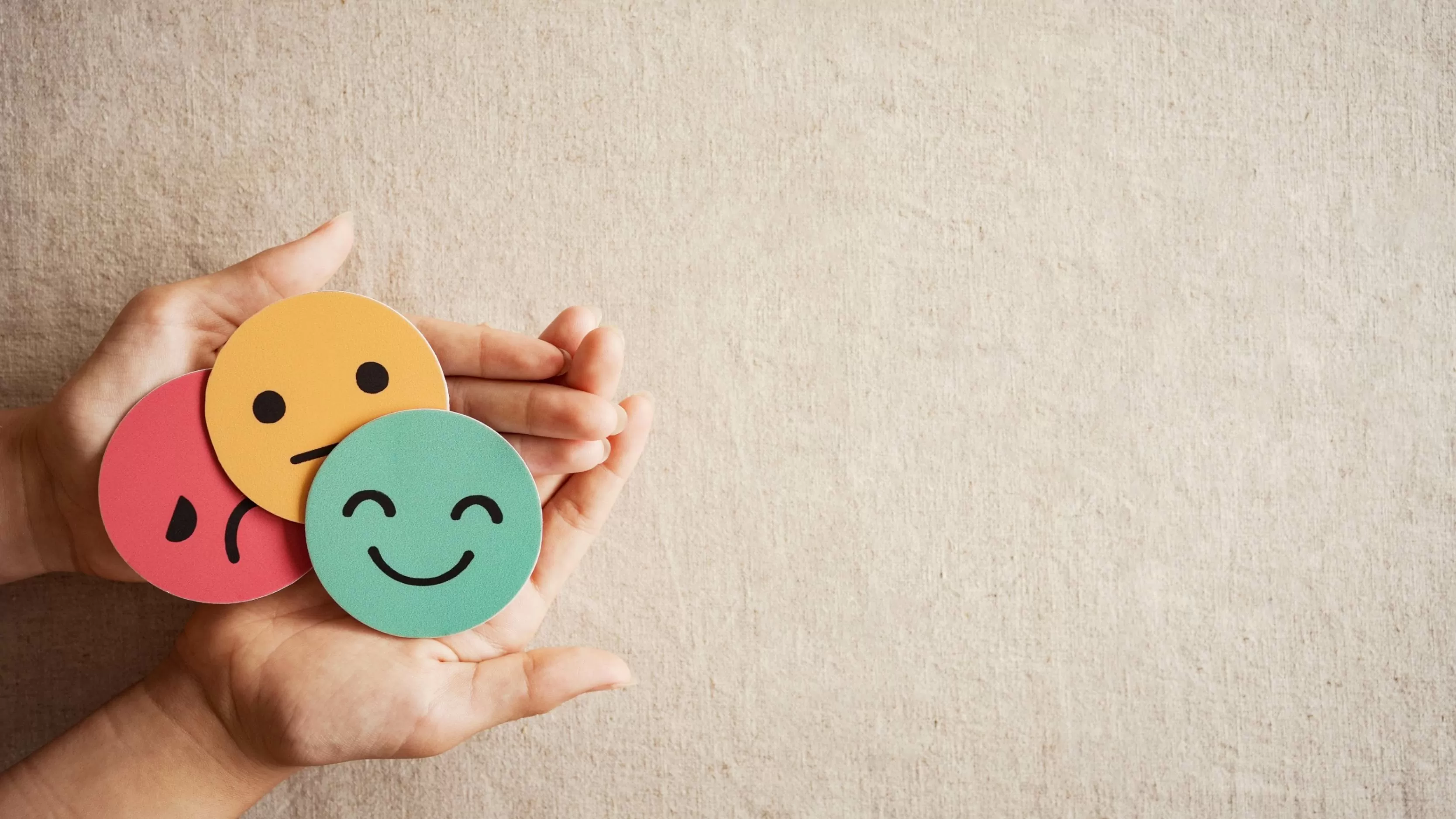 Manos que sostienen caras de papel con emociones diversas triste, feliz y neutra 