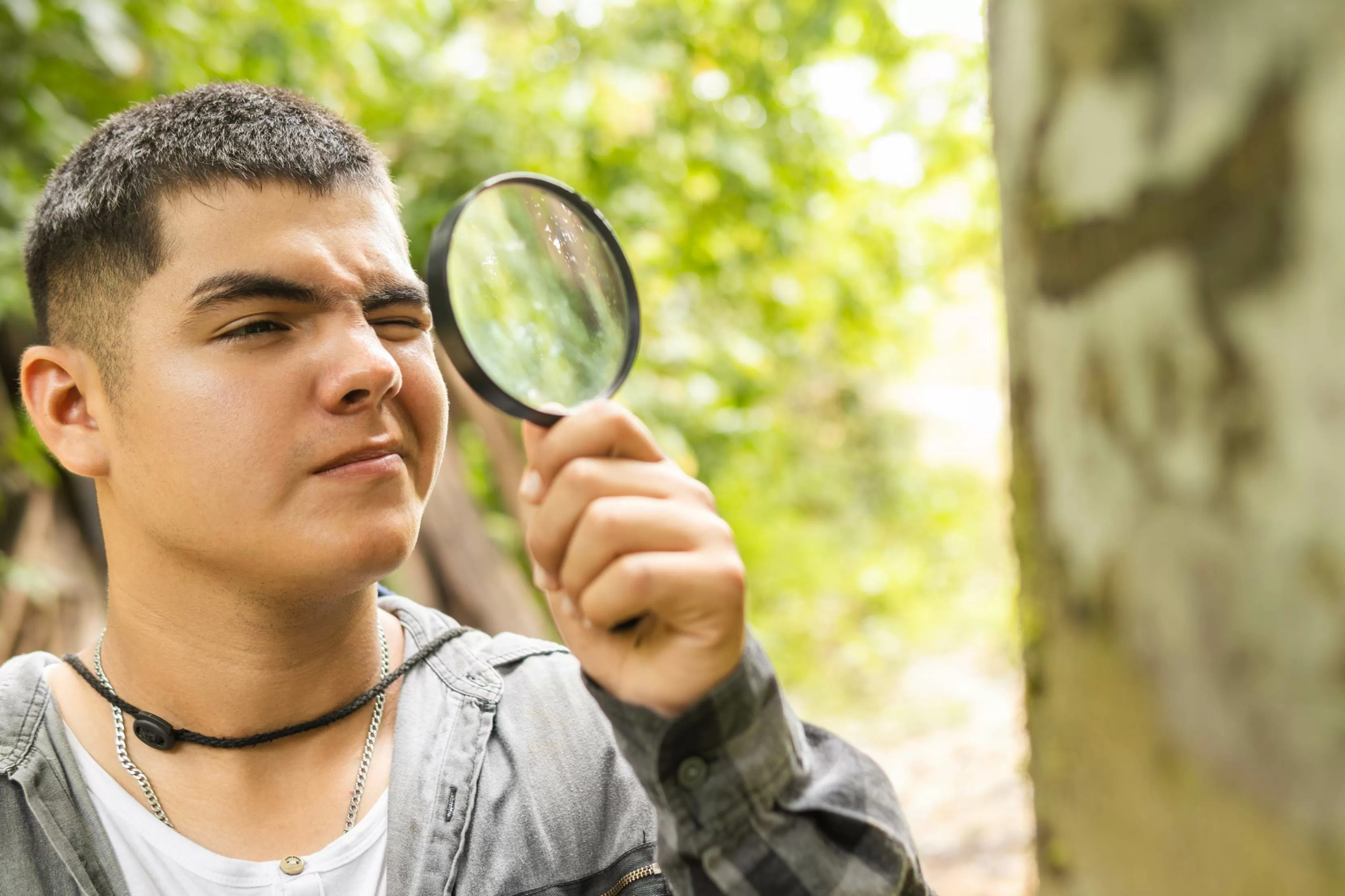 Un jjoven sostiene una lupa mientras observa en medio de la naturaleza