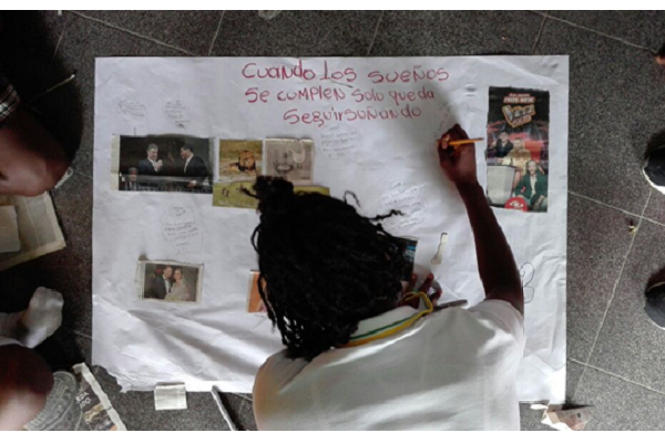 Joven escribe en un cartel "cuando los sueños se cumplen, solo queda seguir soñando" 