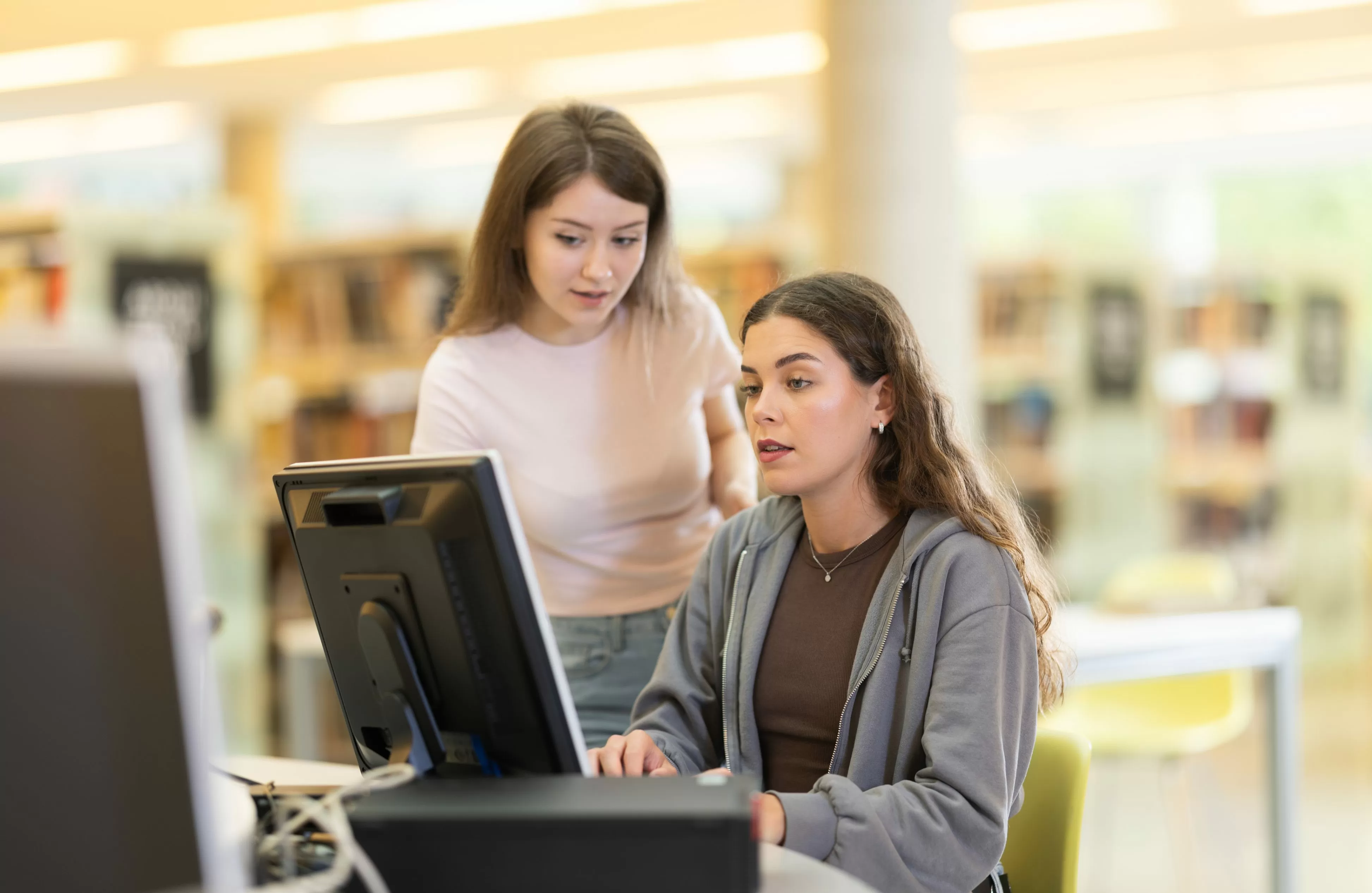 Joven referencista ayudando a una estudiante a trabajar en la computadora en la Biblioteca