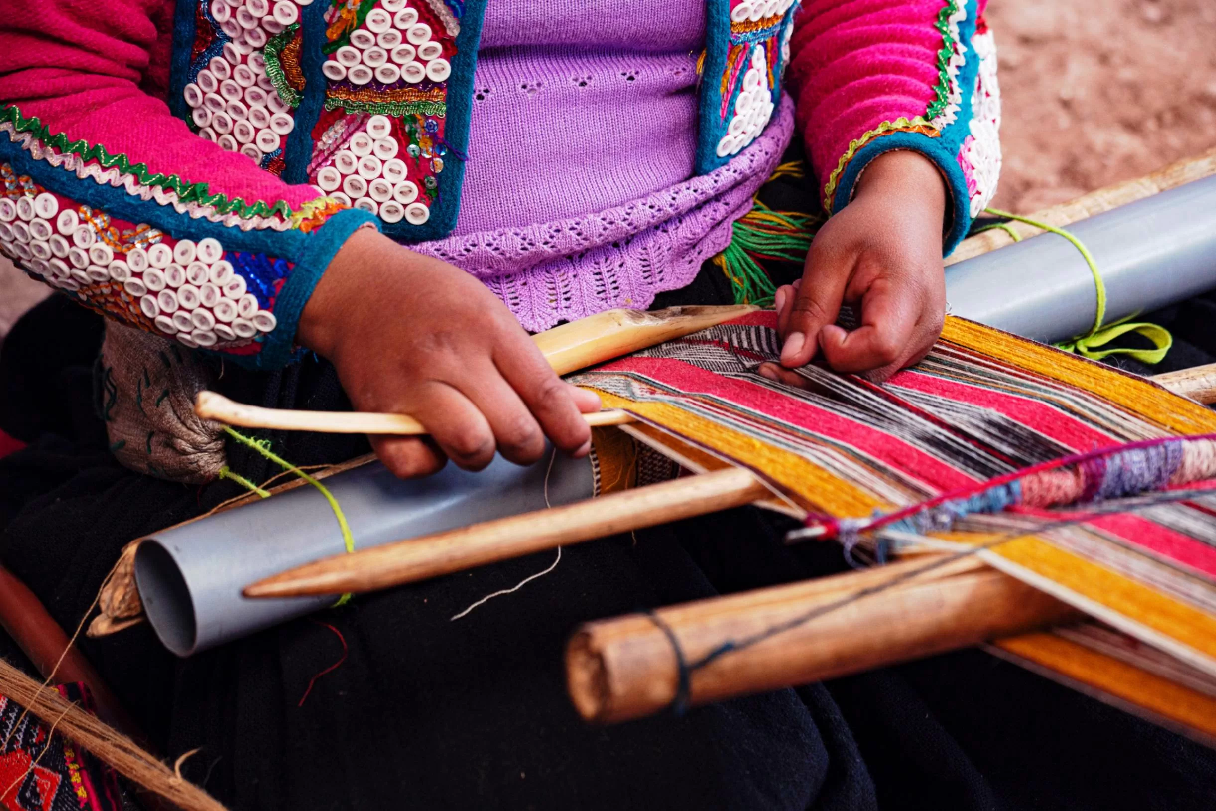 Plano cerrado de las manos de una mujer tejiendo en un telar hilos de multiples colores